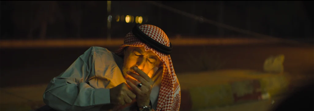A man in a red-and-white keffiyeh lighting a cigarette, his face illuminated by the flame.
