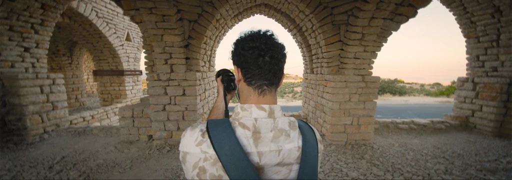 A photographer seen from behind beneath stone arches in warm evening light.